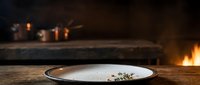 Empty plate with herbs on rustic wooden table, warm fireplace glow in background, suitable for restaurant menus, food blogs, culinary content.