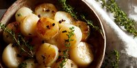 Roasted baby potatoes seasoned with fresh thyme and black pepper in rustic pan, close up view with natural lighting and soft shadows.