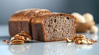 Fresh sliced homemade whole grain bread with walnuts and seeds on light surface against dark background, showing detailed crumb texture and crust.