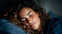 Young woman with curly hair sleeping peacefully in bed with soft morning light creating warm atmosphere for wellness and rest concepts.