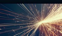 Bright sparks and light trails explode against dark background creating dynamic starburst effect with glowing orange and yellow streaks radiating from central point.