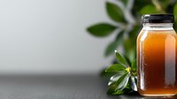 Fresh amber honey in glass jar with green leaves on gray background, showcasing natural sweetener for food packaging and healthy lifestyle content.