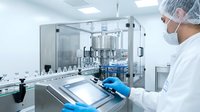 Pharmaceutical technician in protective gear operating automated bottling equipment in sterile manufacturing facility for drug production and quality control.