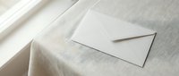 White envelope on beige linen fabric with soft natural lighting creating elegant shadows for stationery and correspondence design projects.