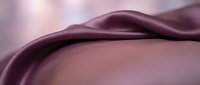 Smooth burgundy satin fabric with flowing waves and soft folds, showcasing luxurious texture and elegant drape in warm mauve tones.