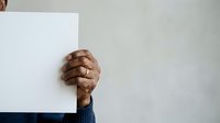 Male hand with medium brown skin tone holding blank white paper or card against neutral background, suitable for advertising, messaging, announcements, and promotional campaigns.