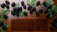 Ripe blackberries with green leaves arranged on wooden surface, flat lay composition for food styling and culinary content.