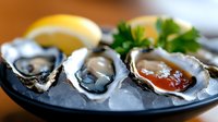 Fresh oysters served on crushed ice with lemon wedges, parsley garnish and red cocktail sauce on black plate, close up view of luxury seafood appetizer.
