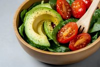 Fresh avocado and cherry tomato salad in wooden bowl with spinach leaves and black pepper seasoning for healthy eating and nutrition concepts.
