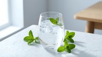 Refreshing glass of sparkling water with fresh mint leaves and ice cubes on marble surface in bright modern kitchen setting for healthy lifestyle.