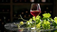 Red wine glass with fresh grape vine leaves on dark stone surface for elegant dining and vineyard themes.