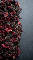 Dried hibiscus flowers and tea leaves blend in rich crimson and dark tones against neutral background, ideal for beverage, wellness and culinary design projects.