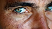 Close-up macro shot of intense blue eyes with detailed iris pattern, long eyelashes, and natural skin texture showing pores and facial features in sharp focus.