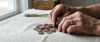 Senior adult hands counting coins on table, representing financial planning, savings, and retirement budgeting for older generations.