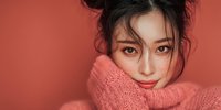 Young Asian woman in cozy coral sweater with messy bun hairstyle against matching background for fashion and lifestyle content.