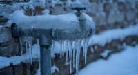 Frozen water pipe with icicles hanging down during winter freeze, showing ice formation and potential plumbing damage from cold weather conditions.
