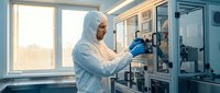 Laboratory technician in protective suit conducting scientific research with automated equipment in sterile cleanroom environment for pharmaceutical development.