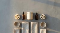 Flat lay composition with amber glass bottles, cream jar, wooden slices, and natural elements arranged symmetrically on neutral background for skincare, wellness, or cosmetic branding projects.