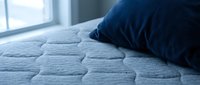 Close-up of blue pillow on quilted mattress surface with natural window light, suitable for bedding, sleep wellness, and home decor design projects.