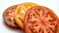 Sliced ripe tomatoes in various shades from orange to red, displaying fresh seeds and juice, suitable for food photography and culinary designs.
