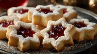 Homemade star-shaped cookies with red jam filling and powdered sugar dusting on dark plate, festive holiday baking treat.