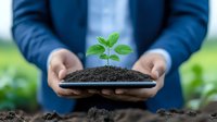 Young green sprout growing in soil on plate held by Asian businessman in blue suit, symbolizing sustainable business growth and environmental responsibility.