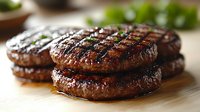 Grilled beef burger patties with charred grill marks and juicy texture on wooden cutting board, close-up view showing caramelized meat surface and cooking details.