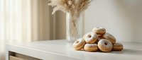 Fresh homemade donuts with sugar coating arranged on white kitchen counter in bright modern interior with pampas grass decoration for bakery display.