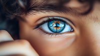 Close-up macro shot of bright blue eye with brown central heterochromia, long eyelashes and smooth skin texture showing intricate iris details and reflection.