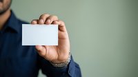 Man in dark blue shirt holding blank white business card for corporate branding and professional networking purposes.