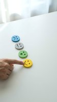 Hand selecting yellow smiley face button among blue, gray, and green emotion faces on white surface. Customer satisfaction, feedback, and positive rating concept for business and service evaluation.