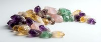 Collection of colorful raw gemstones including amethyst, citrine, rose quartz and green fluorite crystals scattered on white background for jewelry making.
