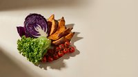 Fresh organic vegetables arranged in colorful display featuring purple cabbage, green kale, cherry tomatoes and sweet potato wedges for healthy cooking.