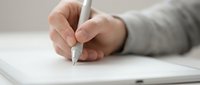 Close-up of a hand writing on paper with a stylus pen, capturing a productive work or study moment on a clean white desk.