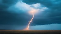 Dramatic lightning bolt strikes across turquoise stormy sky over empty prairie landscape during thunderstorm, creating powerful natural phenomenon display.