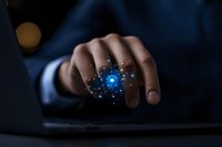 Male hand touching glowing blue digital particle effect above laptop keyboard in dark room, representing digital transformation and future technology.