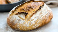 Freshly baked artisan sourdough bread loaf with golden crust and flour dusting on rustic kitchen counter for bakery and homemade cooking concepts.