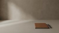Closed brown leather notebook with pen on minimalist beige surface with soft natural light and shadow, suitable for business, education, and stationery design projects.