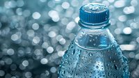 Condensation droplets on cold water bottle surface with blue cap against blurred bokeh background, fresh drink concept for advertising and packaging design.