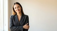 Professional young Caucasian businesswoman in dark suit smiling confidently with crossed arms in modern office interior for corporate presentations.