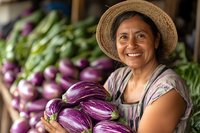 Smiling mature woman in straw hat holding fresh purple eggplants at local market with colorful vegetables in background. Authentic farm-to-table concept.