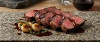 Sliced medium-rare beef steak with roasted potatoes and herbs on stone plate, gourmet dinner presentation for restaurant menu and culinary advertising.