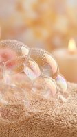 Delicate soap bubbles with rainbow reflections floating on soft towel surface creating dreamy spa atmosphere with warm golden bokeh background.
