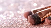 Professional makeup brushes with rose gold glitter background, soft focus bokeh effect creates luxurious cosmetic atmosphere for beauty and fashion industry.