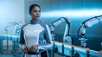 Young African American female engineer working with robotic arms in modern automated manufacturing facility with blue lighting and advanced technology.