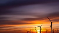 Wind turbines silhouetted against dramatic sunset sky with orange and purple clouds. Renewable energy concept for sustainable power generation and clean technology.