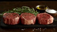 Raw beef tenderloin steaks with fresh rosemary, olive oil and sea salt on dark stone board, ready for cooking. Perfect for food photography and menus.