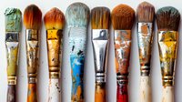 Row of old used paintbrushes showing wear and tear with paint stains, distressed wooden handles and metal ferrules arranged in artistic composition.