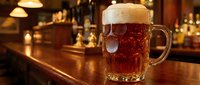 Fresh pint of amber beer with foam head on wooden bar counter in traditional pub setting with warm lighting and blurred background atmosphere.