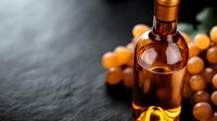 Amber glass bottle with golden liquid surrounded by fresh grapes on dark stone background, selective focus with copy space. Elegant wine or spirits concept.